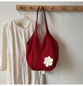 Detail of red crochet tote bag featuring white floral accent and open weave texture