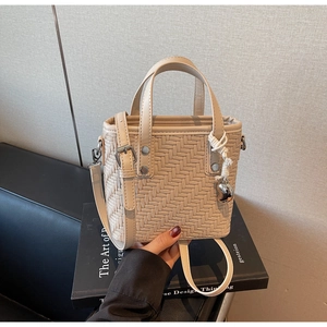 Dettaglio borsa a tracolla intrecciata beige su libro con ciondolo a cuore