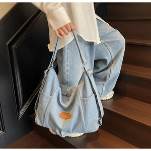 Close-up of light blue denim tote bag with brown leather logo tag and wide shoulder strap