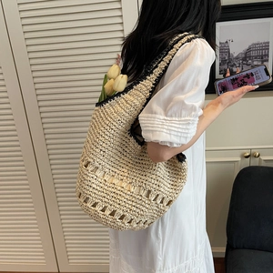 Detail of large straw tote bag with black trim worn on shoulder in a minimalist room