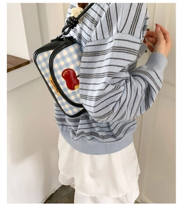 Detail of blue plaid shoulder bag featuring a red apple patch and black leather trim