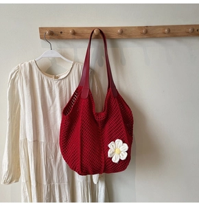 Detail of red crochet tote bag with white flower decoration hanging on wooden hook