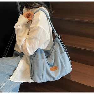 Detail of light blue denim tote bag with brown leather patch on a casual shoulder bag