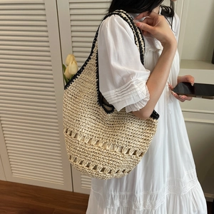 Detail of straw tote bag showing natural fiber weave and black edge trim on a model