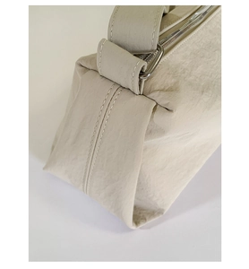 Detailed close-up of cream-colored wrinkled fabric texture and metal buckle on handbag