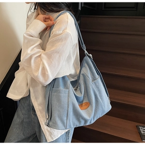Detail of light blue denim tote bag with brown leather logo patch worn by a model