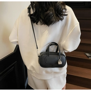 Detail of black litchi leather mini bowling bag worn crossbody by a model in soft lighting