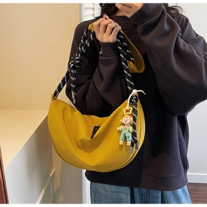 Detalle de bolso media luna amarillo con correa de cuerda y colgante de dibujos