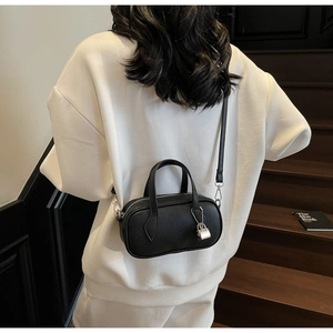 Detail of black pebbled leather crossbody bag with silver lock charm on white sweater