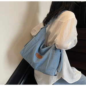 Close-up of a blue denim tote bag with a leather logo patch and wide shoulder strap