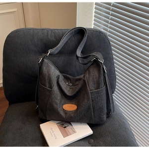 Detail of dark grey canvas shoulder bag with brown leather patch and side zipper pocket