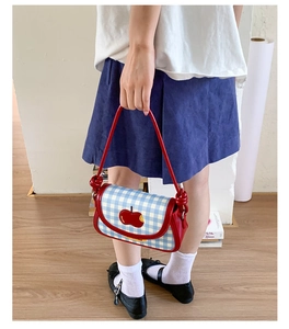 Detail of blue gingham crossbody bag with red leather handle and 3D apple applique