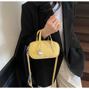 Detail of yellow lychee grain pillow bag featuring a silver lock charm and adjustable strap
