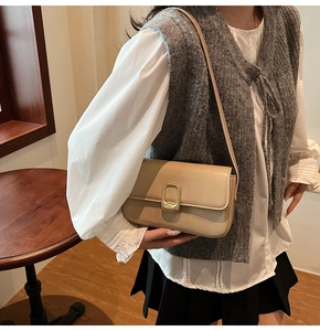 Detalle de un bolso bandolera de cuero mate beige con hebilla de metal dorada en forma de U