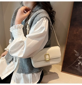 Detalle de bolso baguette blanco con hebilla dorada al hombro de una modelo elegante