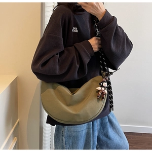 Detalle del bolso de lona verde militar en forma de media luna con correa de cuerda y muñeco
