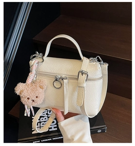 Detailed view of white embossed leather bucket bag with a cute brown plush bear charm