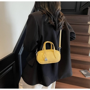 Detail of bright yellow pebble leather pillow bag with silver lock charm on black background