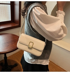 Detalle de un bolso de hombro rectangular blanco crema con hebilla dorada en una modelo