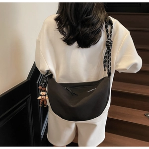 Detalle de bolso bandolera de lona negra con correa tejida y colgante decorativo