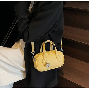 Close-up of a bright yellow litchi grain handbag with silver lock on wooden stairs