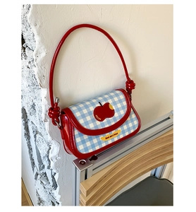 Close-up of red plaid shoulder bag featuring glossy patent leather and apple embroidery