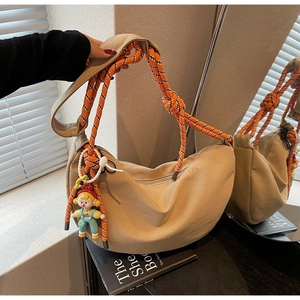 Detalle de bolso hobo beige con correa tejida naranja gruesa y colgante de muñeco pequeño