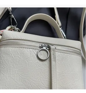Close-up of smooth metal zipper and ring pull on cream crinkled texture handbag