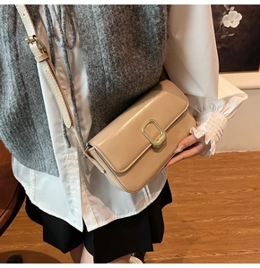Detalle de un bolso de hombro en cuero beige con hebilla dorada llevado por una modelo