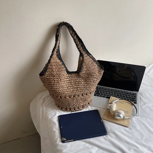 Detail of a woven straw tote bag featuring black reinforced edges on a white bedding background