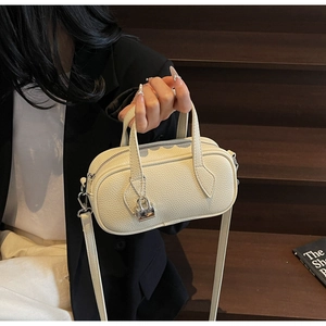 Detail of off-white lychee grain leather pillow bag with silver lock and long strap