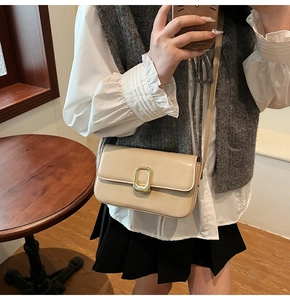 Detalle de bolso bandolera de cuero beige con hebilla rectangular grande de metal dorado