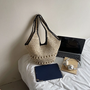 Detail of straw tote bag with black trim and hollow weave on a white fabric surface