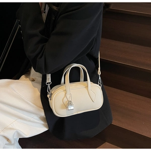 Close-up of beige lychee grain leather crossbody bag held by model on wooden stairs