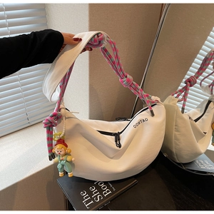 Detalle de bolso bandolera blanco de media luna con correa tejida y colgante de muñeca de dibujos