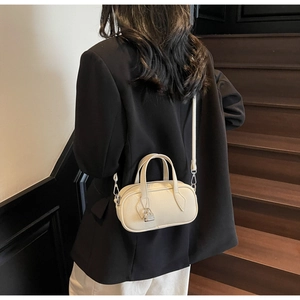 Detail of a beige lychee leather pillow bag with metal lock worn on a black blazer