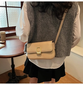 Primer plano de bolso bandolera beige cuadrado con hebilla en U dorada en la mesa