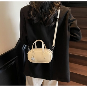 Close-up of beige leather mini pillow bag with metal lock pendant and crossbody strap