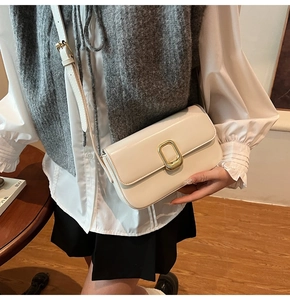 Detalle de un bolso bandolera blanco crema en cuero con hebilla rectangular dorada