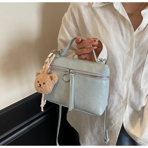 Detail view of ice blue textured leather handbag with silver zippers and bear charm