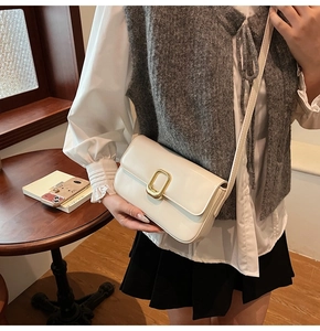 Detalle de un bolso bandolera blanco crema con cierre metálico dorado en una modelo