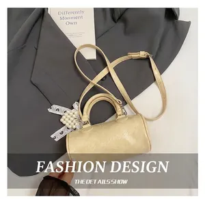 Detail of beige cylinder bag with textured leather, pearl beads and lace bow charm