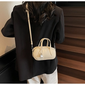 Minimalist beige leather pillow bag with silver lock pendant worn on shoulder over dark suit