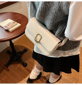 Detalle de un bolso de hombro rectangular blanco crema con hebilla de metal dorado en una mesa