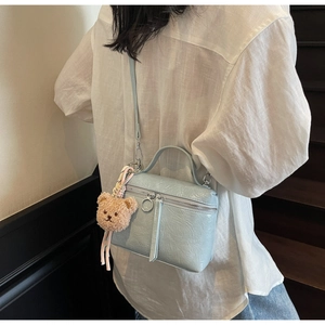Detail of light blue pleated bucket bag with brown plush bear charm worn by a model
