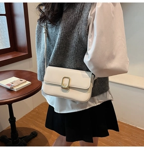 Detalle de un bolso bandolera minimalista en cuero crema con cierre ovalado dorado