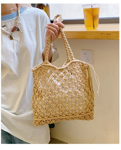 Detail of straw tote bag with woven handles, tassel decor, and drawstring inner lining