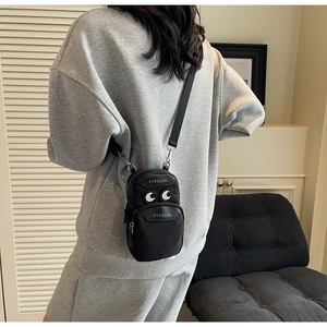 Detail of a black nylon crossbody phone bag with white eyes and TYPAGIRL logo on a model