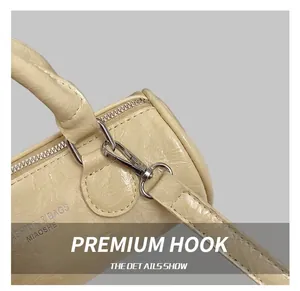 Detail of silver metal hook and strap attachment on beige cylindrical leather bag