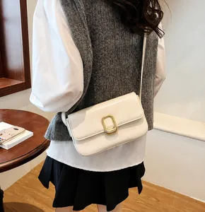 Detalle de un bolso cuadrado de cuero crema minimalista con hebilla de metal dorado